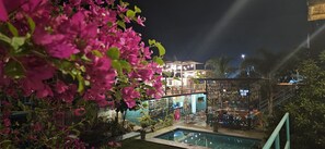Zona de piscina con un área de estar cubierta, un bar y una escalera que conduce a un nivel superior.