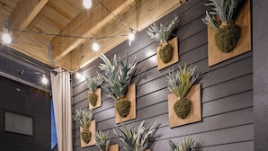 Un intérieur moderne avec un mur en bois foncé, de nombreuses plantes en pot et un canapé noir agrémenté de coussins orange et gris.