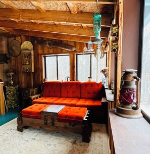 A cozy room with a wooden ceiling, a red sofa, a small table, and a vintage lantern. -  3BR Farmhouse Retreat
Country comfort with farm animals, trails & cozy spaces (Carlton)