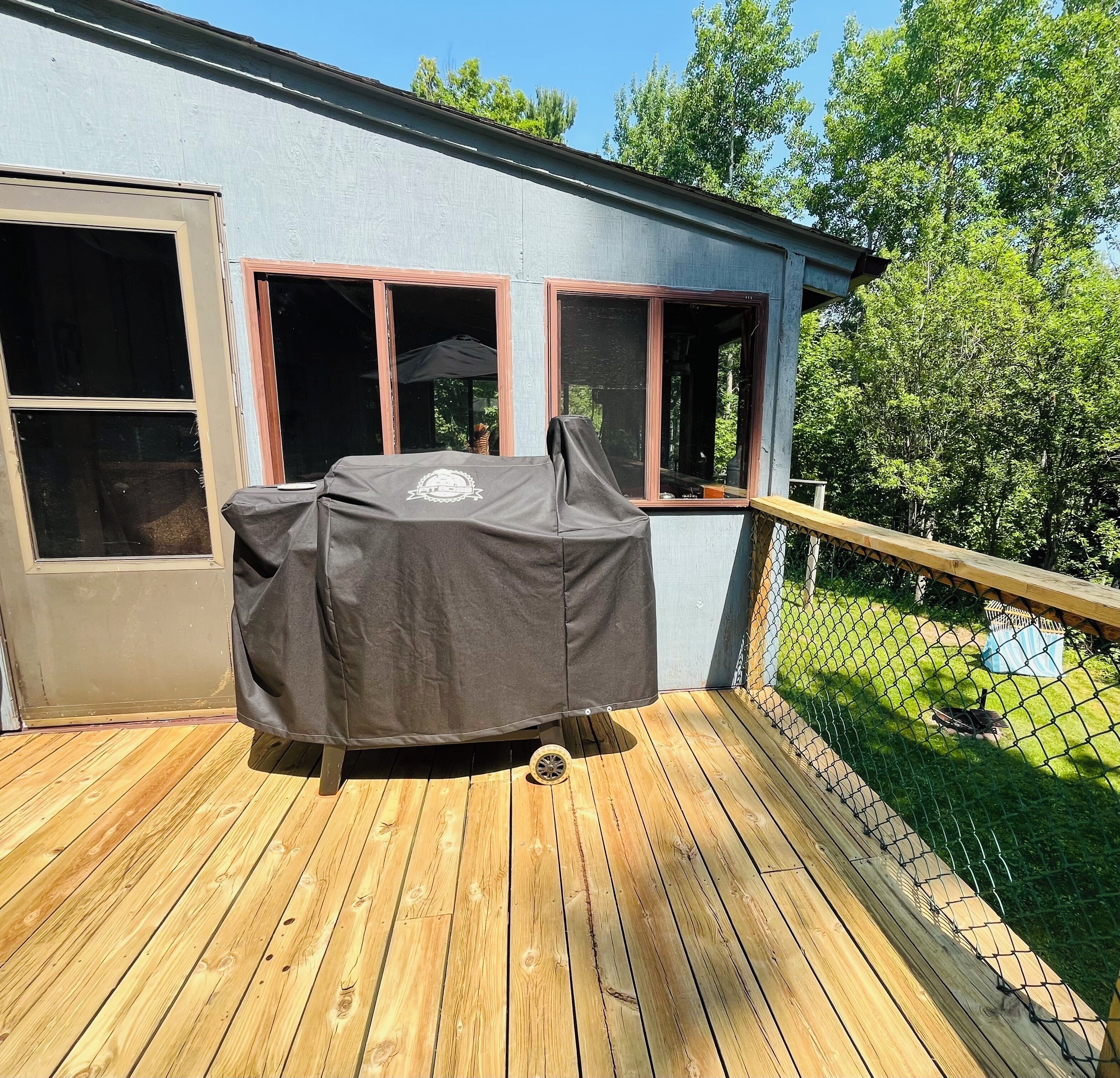 Ein überdachter Grill auf einer Holzterrasse, im Hintergrund ein Haus.