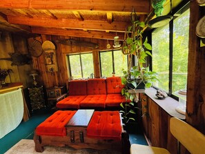 A cozy cabin interior with a wooden ceiling, a red sofa, a wooden table, and a window overlooking greenery. -  3BR Farmhouse Retreat
Country comfort with farm animals, trails & cozy spaces (Carlton)