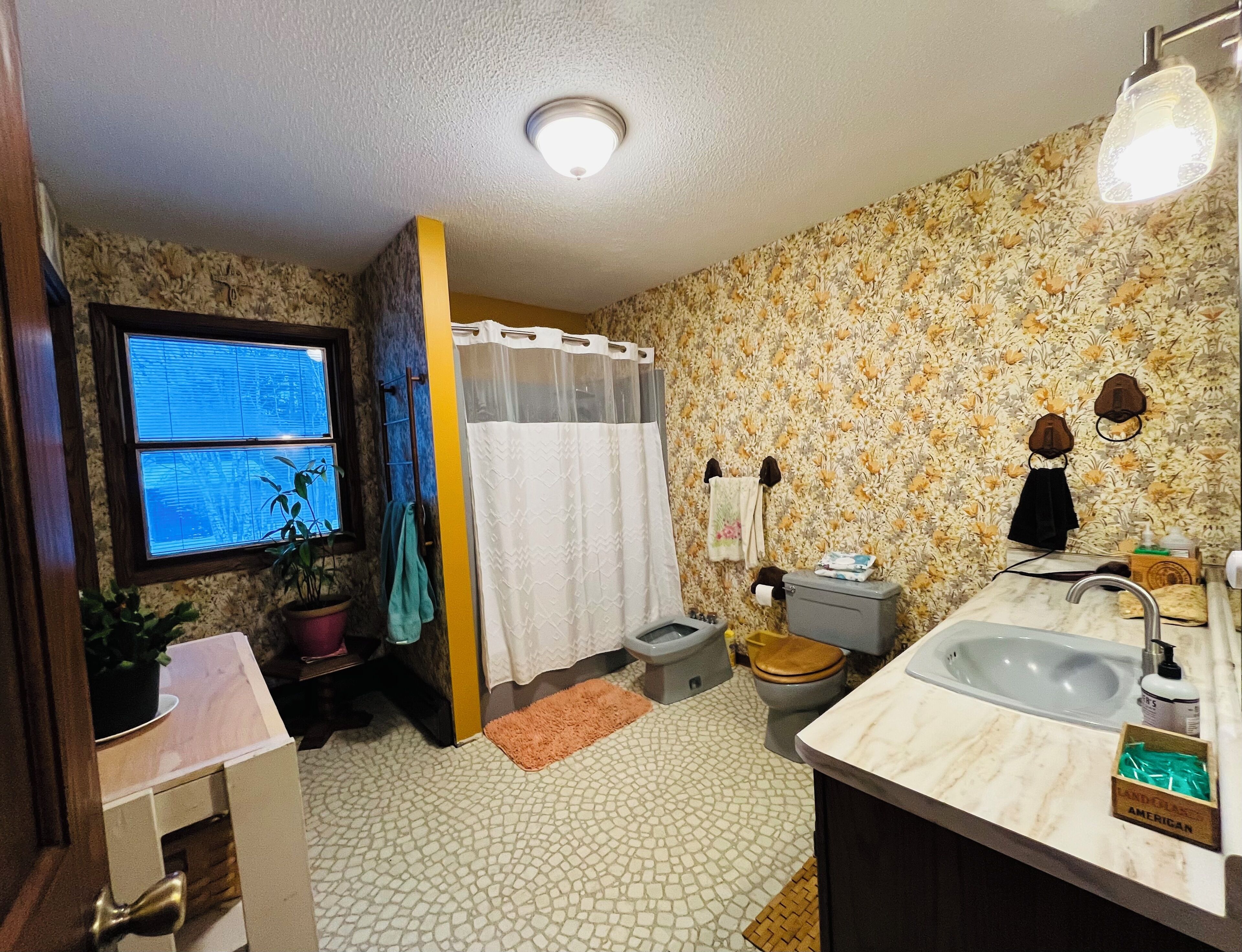 Une salle de bain équipée d’une douche, de toilettes, d’un lavabo et d’une fenêtre avec des stores.