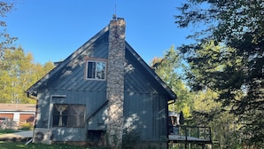 A rustic cabin with a stone chimney, a small window, and a porch with outdoor furniture.