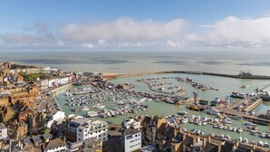 Una località costiera con un porto turistico pieno di imbarcazioni, edifici lungo la passeggiata e una vista limpida sul mare.