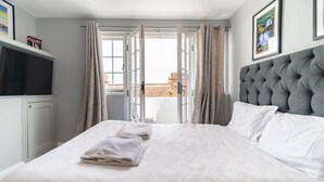 Camera d'albergo con un letto grande, una testiera grigia trapuntata, una televisione su un mobile e vista sulla città attraverso porte aperte.