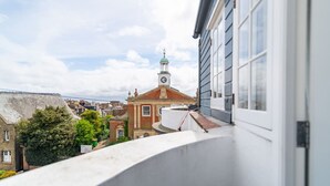 Vista da un balcone su un edificio storico con una torre dell'orologio, circondato da altri edifici e vegetazione.