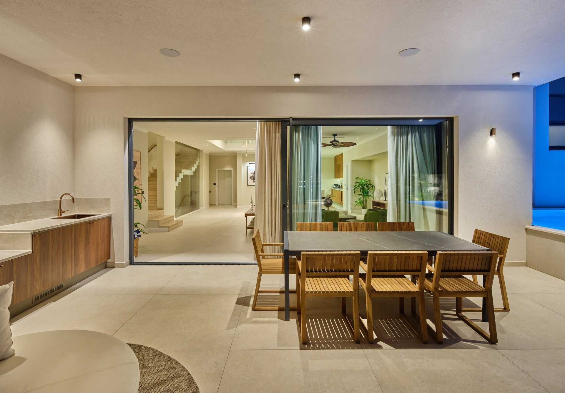 A modern living room with a dining area, a kitchen with a sink, and a staircase leading to another level.