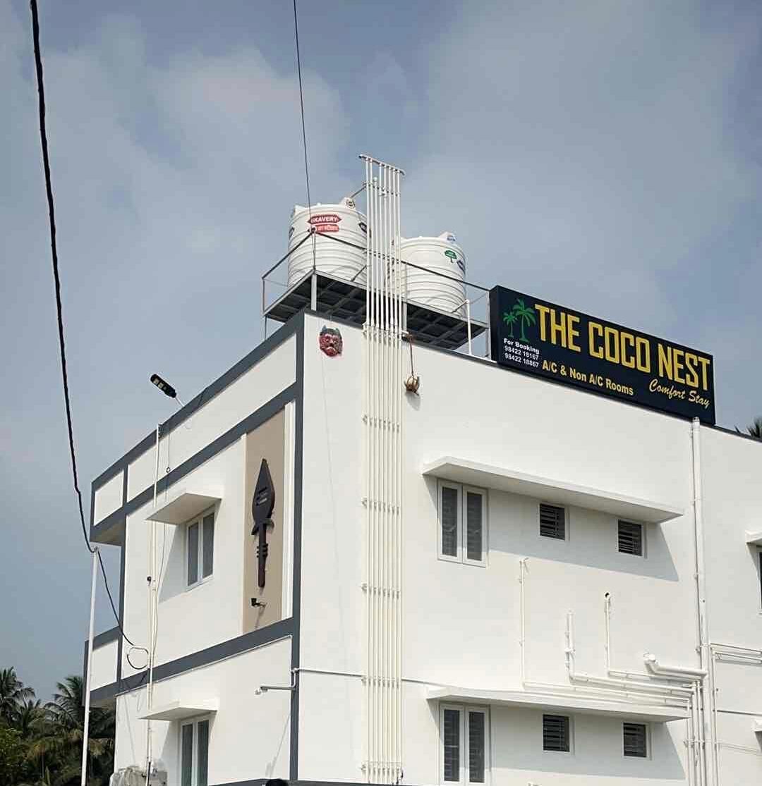 Un edificio con un letrero que dice "The Coco Nest", hotel que ofrece habitaciones con aire acondicionado y sin aire acondicionado, y un número de contacto.