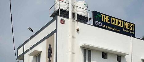 Un edificio con un letrero que dice "The Coco Nest", hotel que ofrece habitaciones con aire acondicionado y sin aire acondicionado, y un número de contacto.