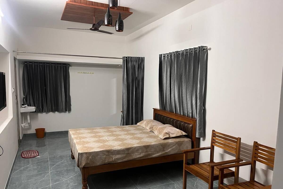 A bedroom with a bed, wooden chairs, a small table, a ceiling fan, and a window with curtains.