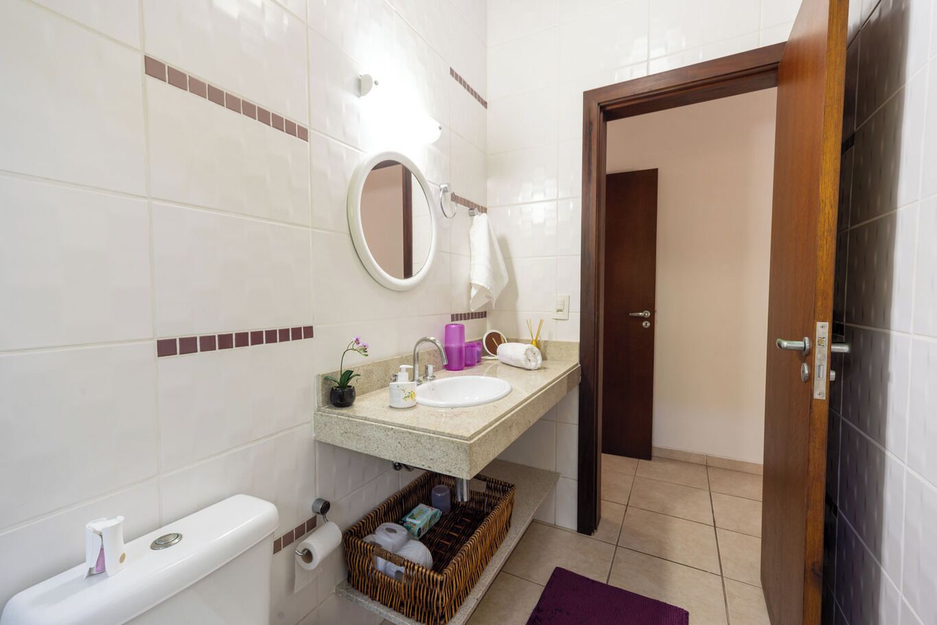 A bathroom with a toilet, sink, mirror, and a basket of toiletries.