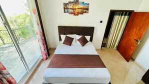 Una camera d'albergo con un letto, vista sul verde attraverso una porta scorrevole e un quadro appeso al muro.