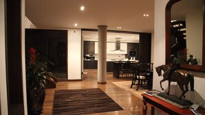 Un intérieur moderne avec un plancher en bois, une colonne centrale, un coin repas avec des chaises et une cuisine en arrière-plan.