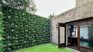 Une maison moderne avec une façade en briques, une pelouse verdoyante et une porte-fenêtre coulissante donnant sur un espace intérieur.