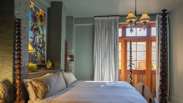 A bedroom with a large bed, a wooden headboard, a painting on the wall, and a window with curtains.