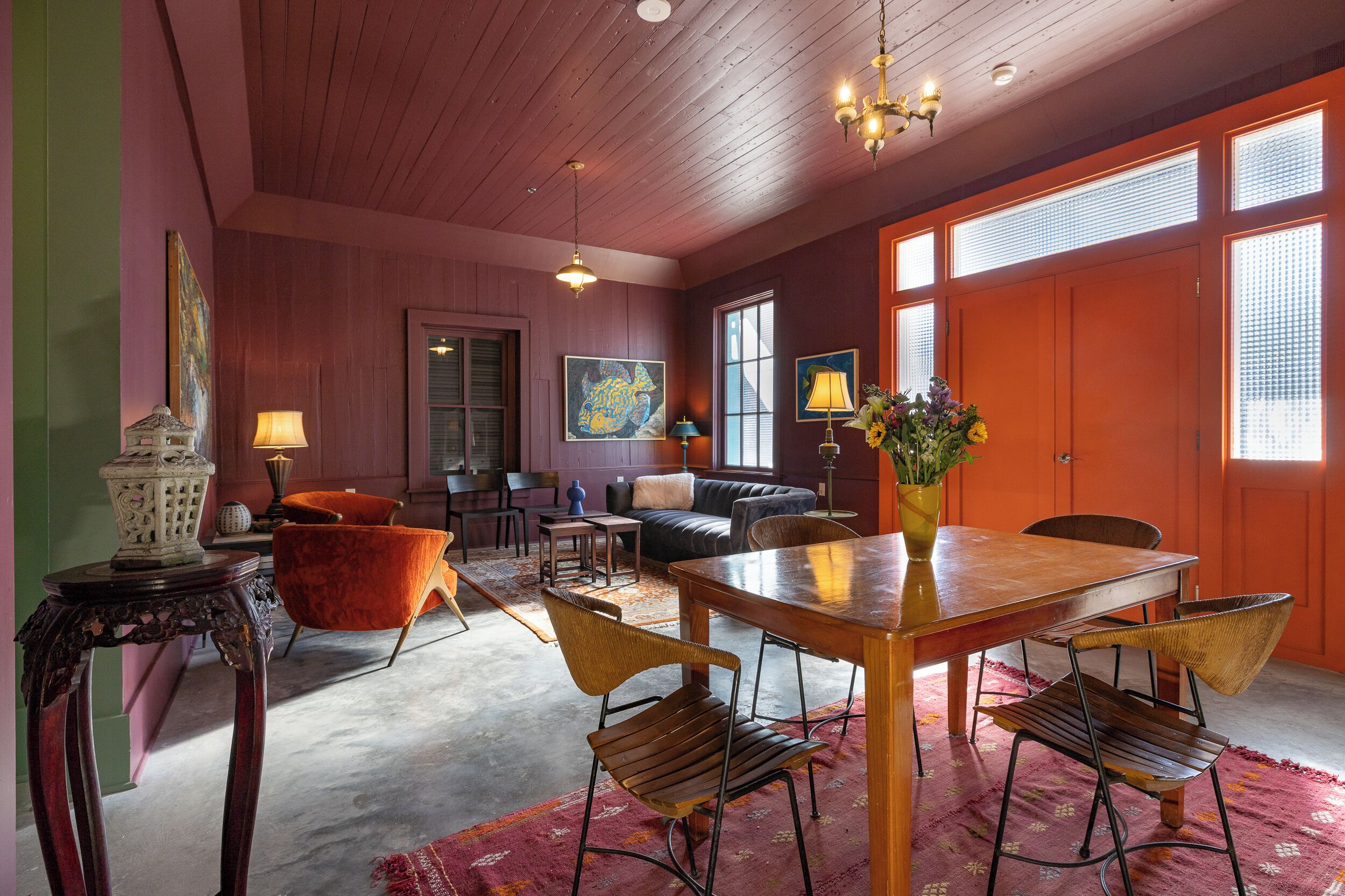 A spacious room with a wooden ceiling, a dining table with chairs, a sofa, and a large window with blinds.