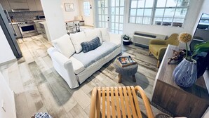A modern living room with a white sofa, a wooden coffee table, and a yellow armchair. There is a kitchen in the background with a built-in oven and microwave. - Beachfront Modern Apt with Direct Sand Access in Sunny Rincon - Villa Sanfe (Rincón)