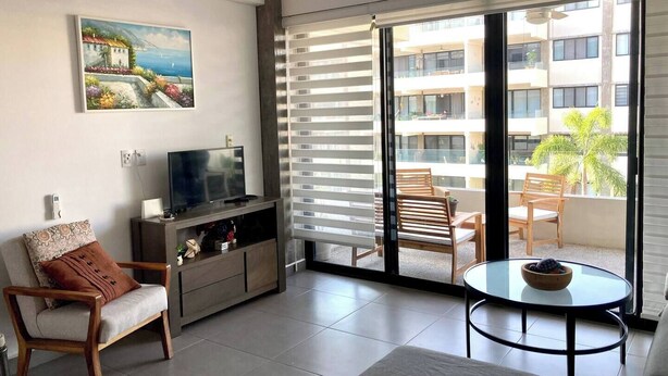 A modern living room with a TV, a sofa, a coffee table, and a balcony with chairs. - Cozy Family Condo - Pool & terrace - 10 minute to the beach - Nuevo Vallarta (Nuevo Vallarta)