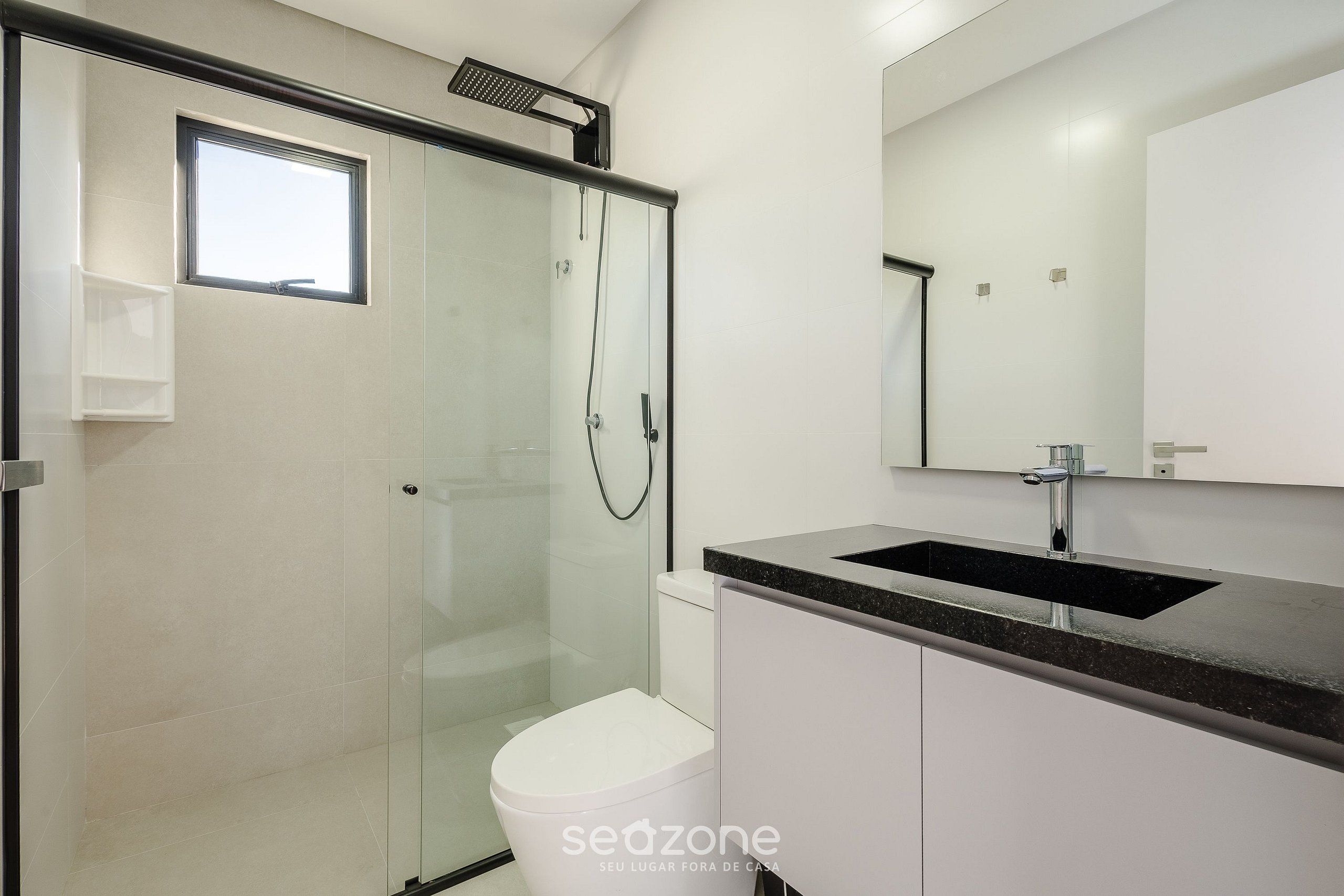 A modern bathroom with a glass shower enclosure, a white toilet, a black countertop sink, and a large mirror above the sink.