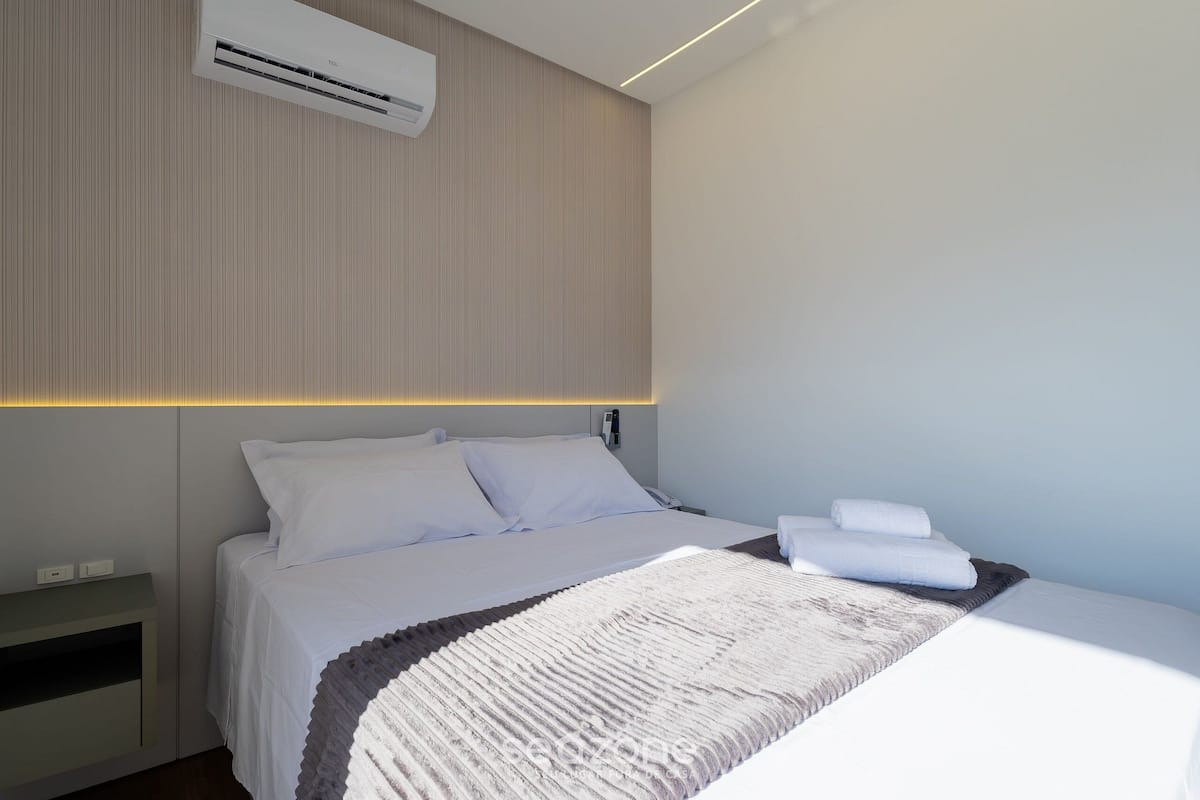 A modern hotel room with a bed, bedside table, and an air conditioning unit.