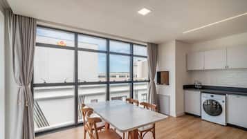 A modern kitchen with a built-in washing machine, a dining area with a table and chairs, and large windows offering a view of the cityscape.
