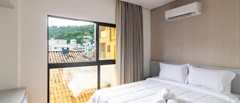 A hotel room with a bed, a window, and an air conditioning unit.