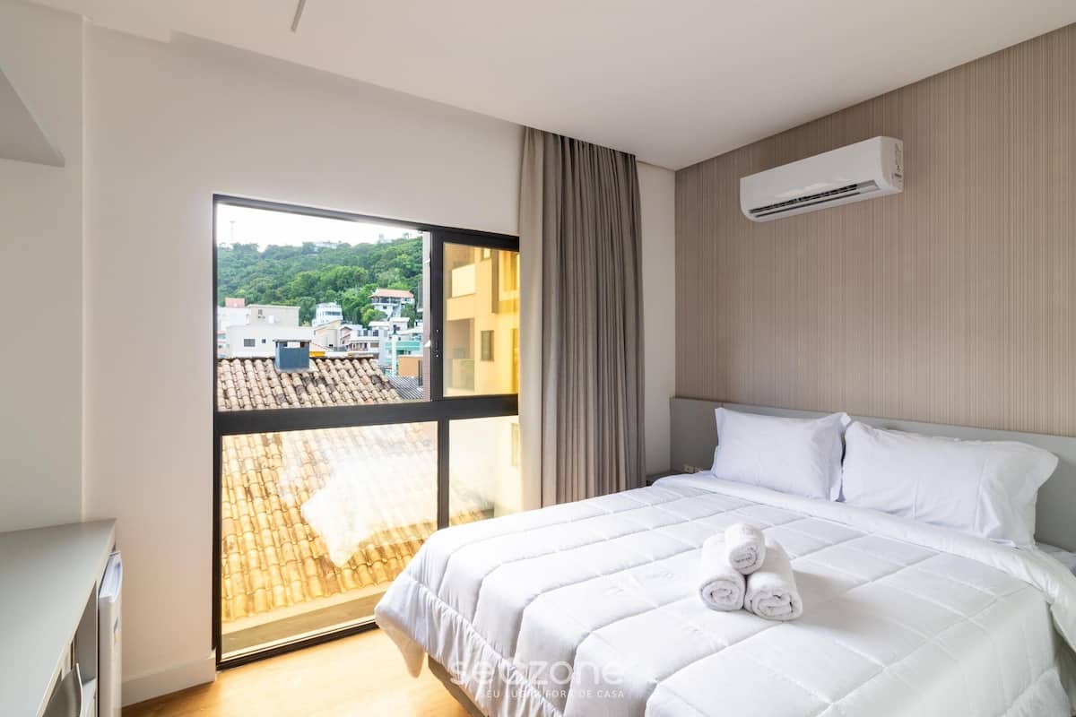 A hotel room with a bed, a window, and an air conditioning unit.