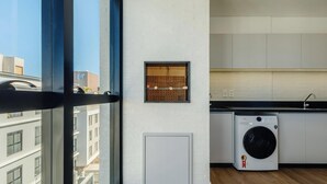Eine moderne Küche mit integriertem Waschmaschinenanschluss, einem Fenster mit Blick auf Gebäude und einer weißen Ziegelwand.