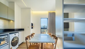 A modern kitchen with a built-in oven and microwave, a dining area with a marble table and wooden chairs, and a view through a large window. - Apartments in a Building With a Pool, 180m From the Beach in Bombinhas - Sfrs (Bombinhas)