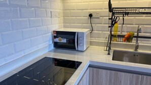 A modern kitchen with white subway tiles, a built-in microwave, a black induction cooktop, and a stainless steel sink with a drying rack. - Cozy 2BR Sky Pool & Panoramic Views 1-6 Guests (Gelugor)