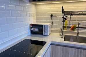 A kitchen with a built-in microwave, a black induction cooktop, and a stainless steel sink with a drying rack. - Cozy 2BR Sky Pool & Panoramic Views 1-6 Guests (Gelugor)