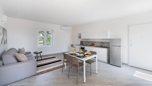 A modern living room with a grey sofa, a dining table set with plates and glasses, and a kitchen area with white cabinets and a refrigerator. - Spacious 2 bedroom apartment with pool (Soiano del Lago)
