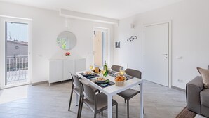 A modern, well-lit dining area with a white table set for two, a white cabinet, and a grey sofa. - Spacious 2 bedroom apartment with pool (Soiano del Lago)