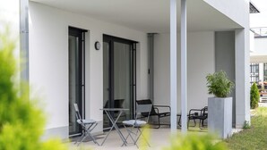 Une terrasse extérieure moderne, avec une table et des chaises, un pot de fleurs et une porte-fenêtre coulissante.