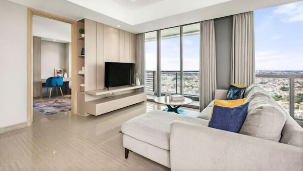 A modern living room with a large window, a flat-screen TV, a sofa, and a dining area. - Fairview House - Luxstay near Airport (Kelapa Dua)