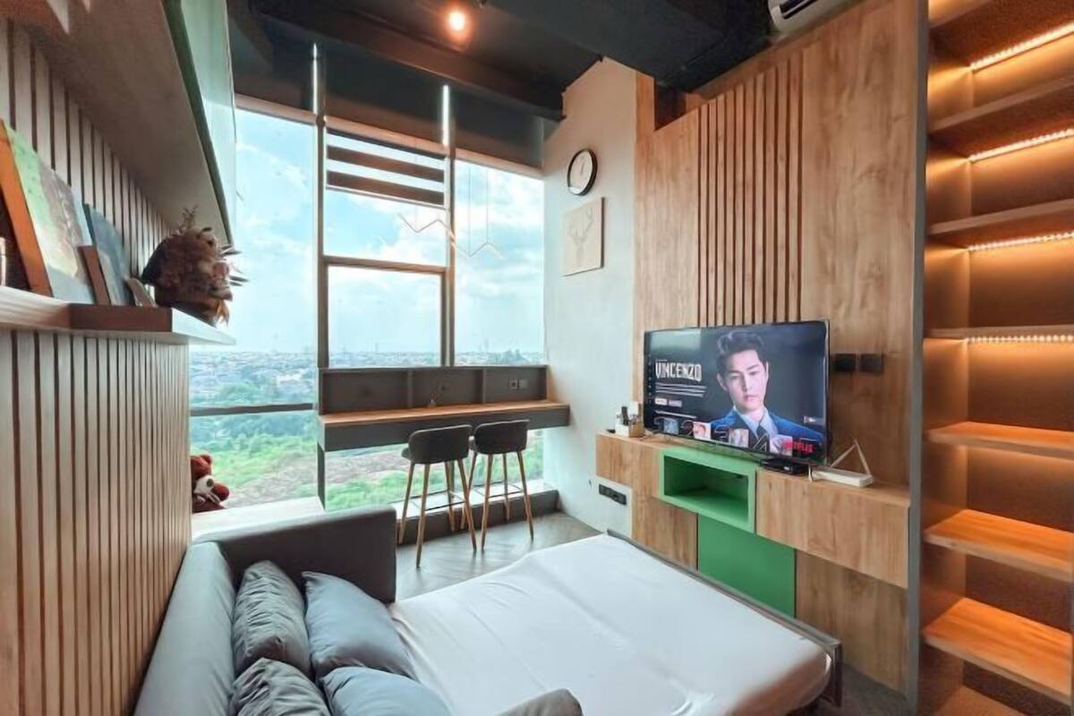 Egy modern szállodaszoba, nagy ablakkal, ággyal, televízióval és egy ülősarokkal.