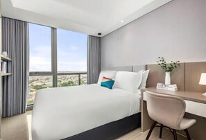 Ein modernes Hotelzimmer mit einem großen Bett, einem Schreibtisch und Blick auf die Stadt.