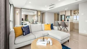 A modern living room with a sectional sofa, a round coffee table, and a kitchen area in the background. - Fairview House - Luxstay near Airport (Kelapa Dua)