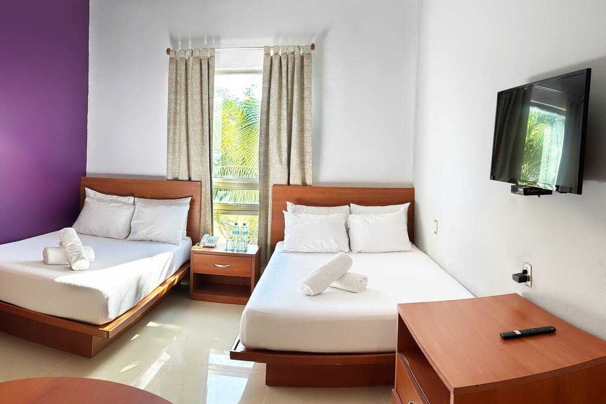 Una habitación de hotel con dos camas, un televisor instalado en la pared y una ventana con cortinas.