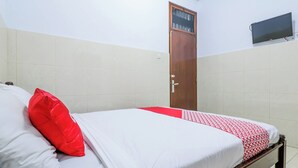 Un lit bien fait, avec une couvre-lit rouge et blanche, un oreiller rouge et une tête de lit en bois.