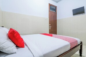 Una cama bien hecha con una colcha roja y blanca, un cojín rojo y un cabecero de madera.