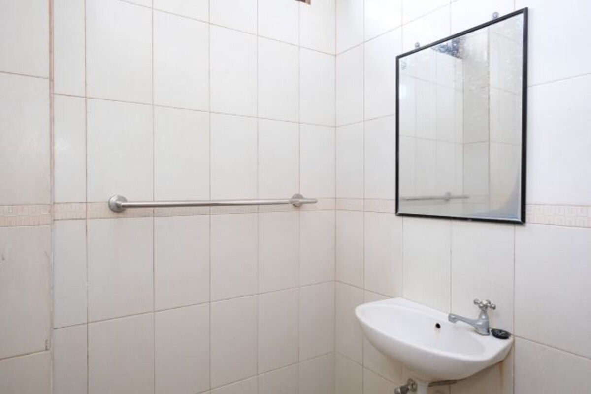 Un baño con azulejos blancos, un lavamanos con grifo, un espejo y una barra de apoyo.