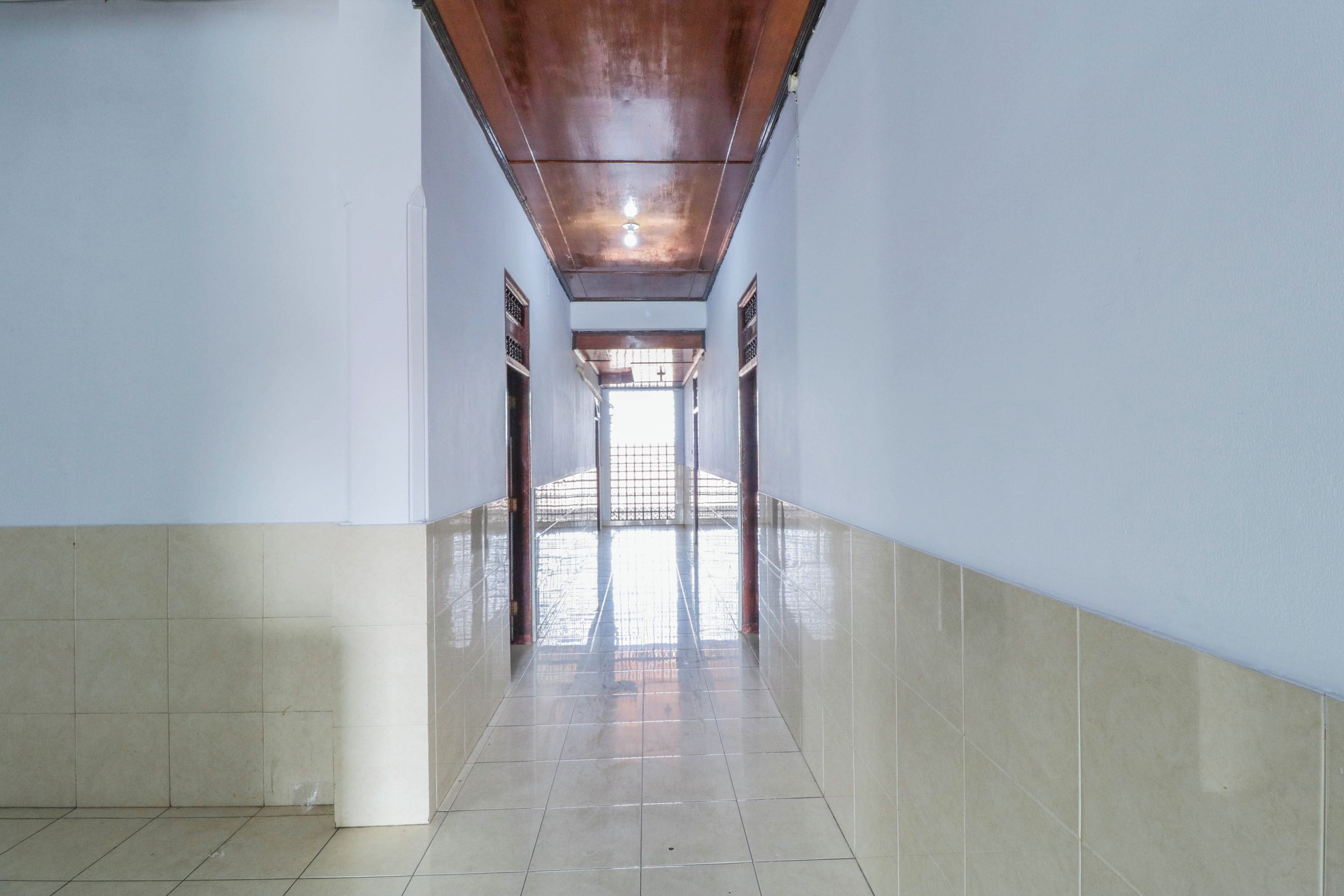 A long, narrow hallway with tiled floors and walls, leading to a bright area with a view through a window.