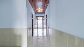 A long, narrow hallway with tiled floors and walls, leading to a bright area with a view through a window.