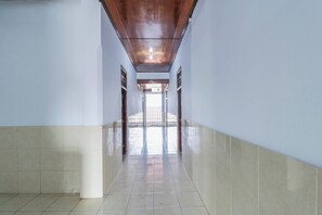 Un pasillo largo y estrecho con pisos y paredes de baldosas, que conduce a un espacio luminoso con vista a través de una ventana.