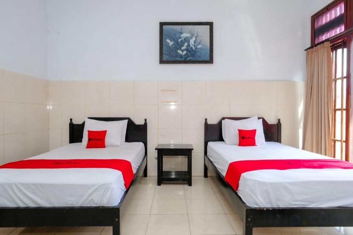 A hotel room with two beds, a small table, and a painting on the wall.