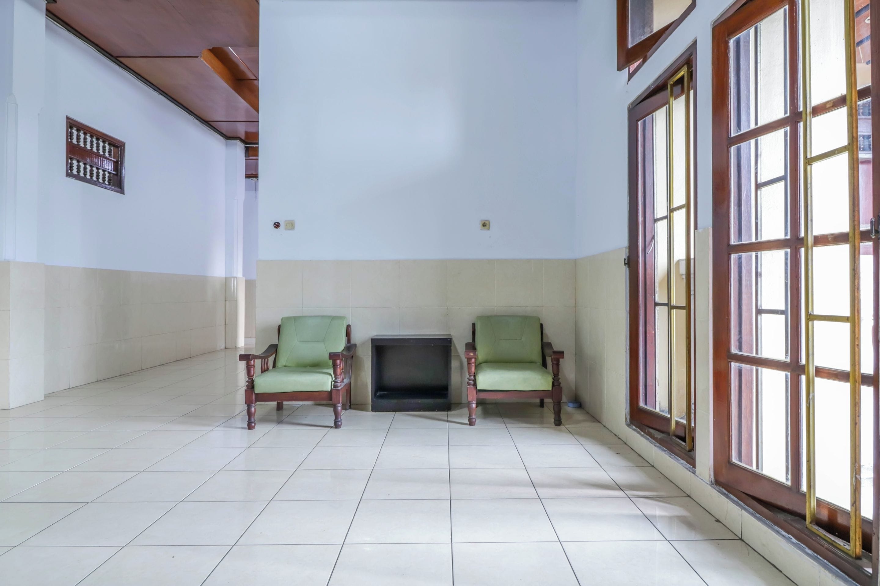 A spacious room with two green armchairs, a fireplace, and large windows with wooden frames.
