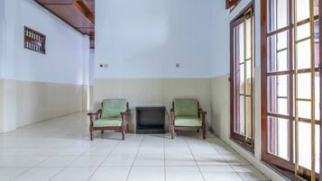 A spacious room with two green armchairs, a fireplace, and large windows with wooden frames.