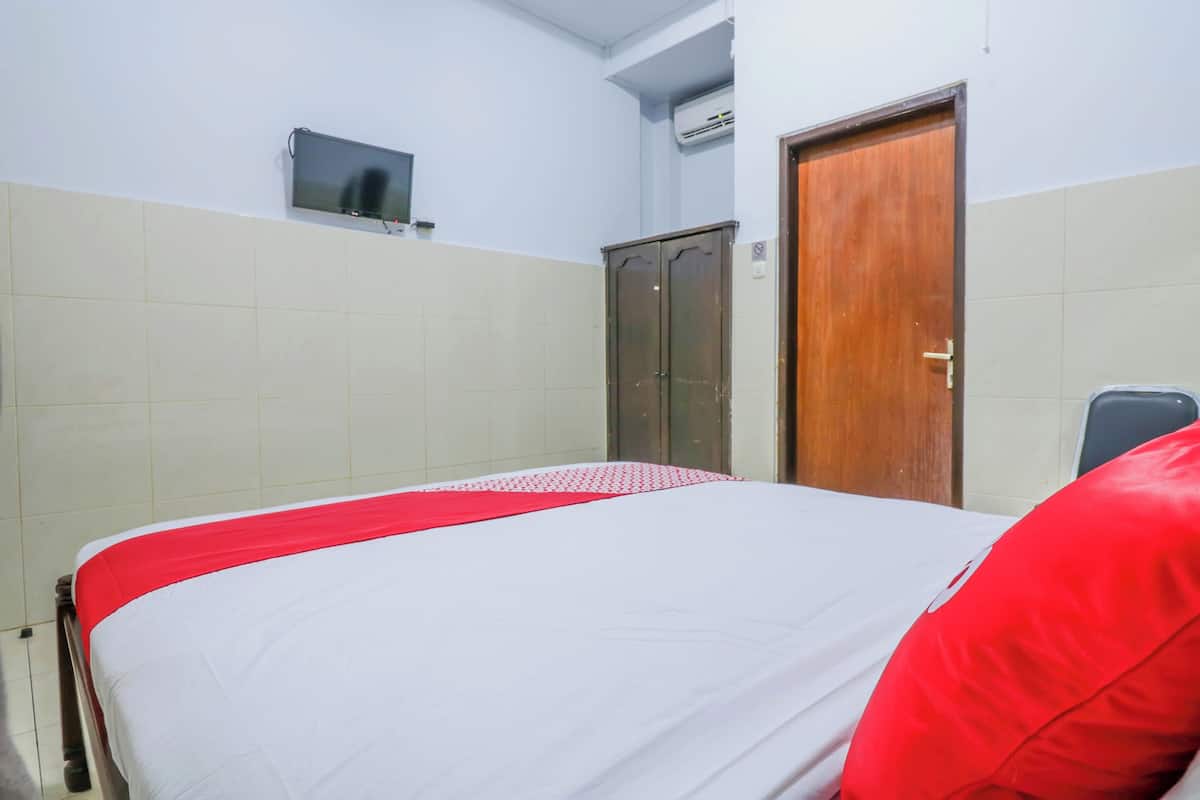 A hotel room with a bed, a television mounted on the wall, a wardrobe, and a door.