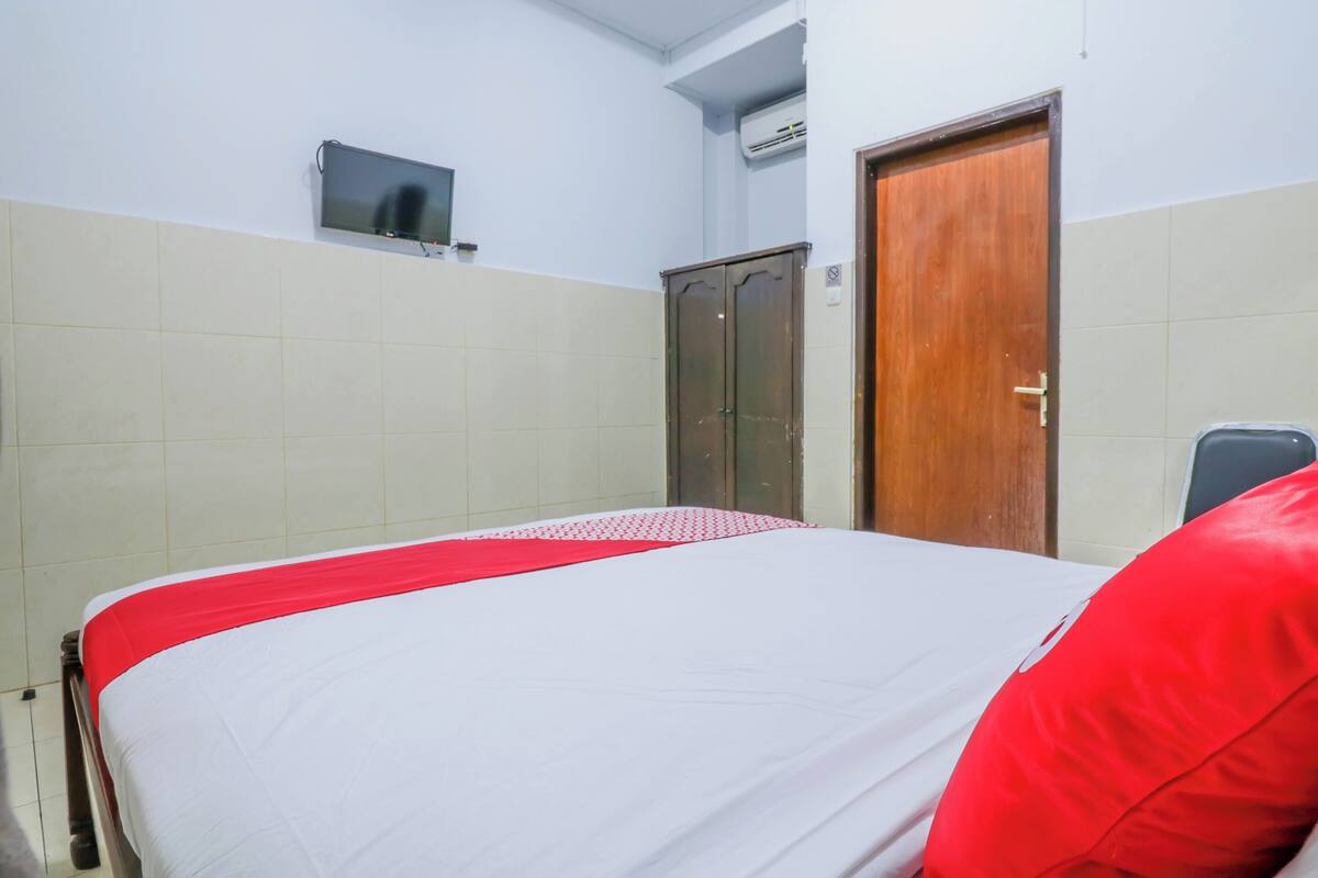 A hotel room with a bed, a wooden wardrobe, a television mounted on the wall, and a door.